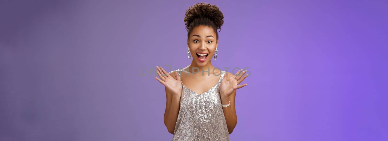 Surprised amused excited african-american woman in glittering shiny silver dress raise hands astonished pleased delighted meeting friend party smiling thrilled standing blue background amazed.
