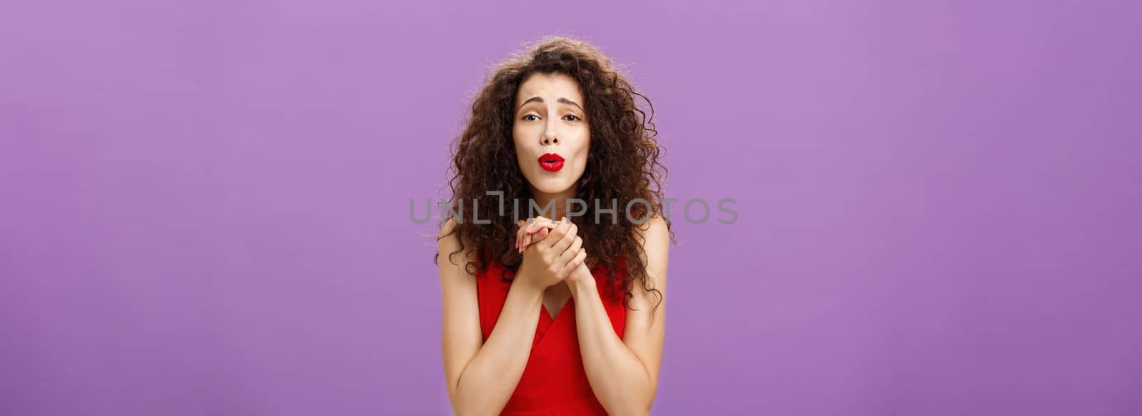 Waist-up shot of woman gazing at heartwarming scene being touched and delighted holding palms togehter over chest folding lips enjoying watching cute puppy posing pleased over purple background by Benzoix