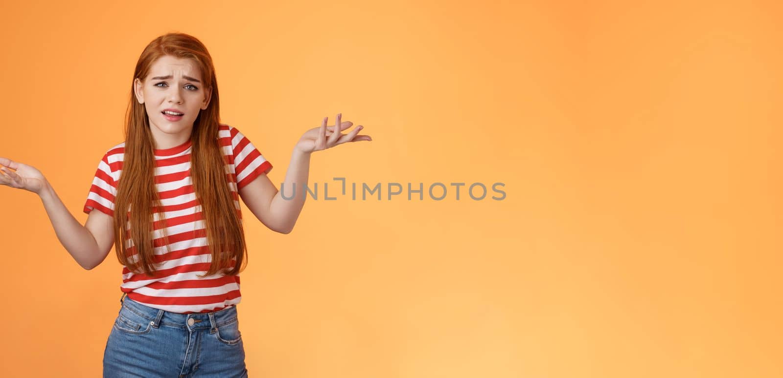 Careless arrogant redhead rich girl say so what, not giving care what people thing, look dismay ignorant shrugging hands spread sideways, uninterested, give no concern, stand orange background.