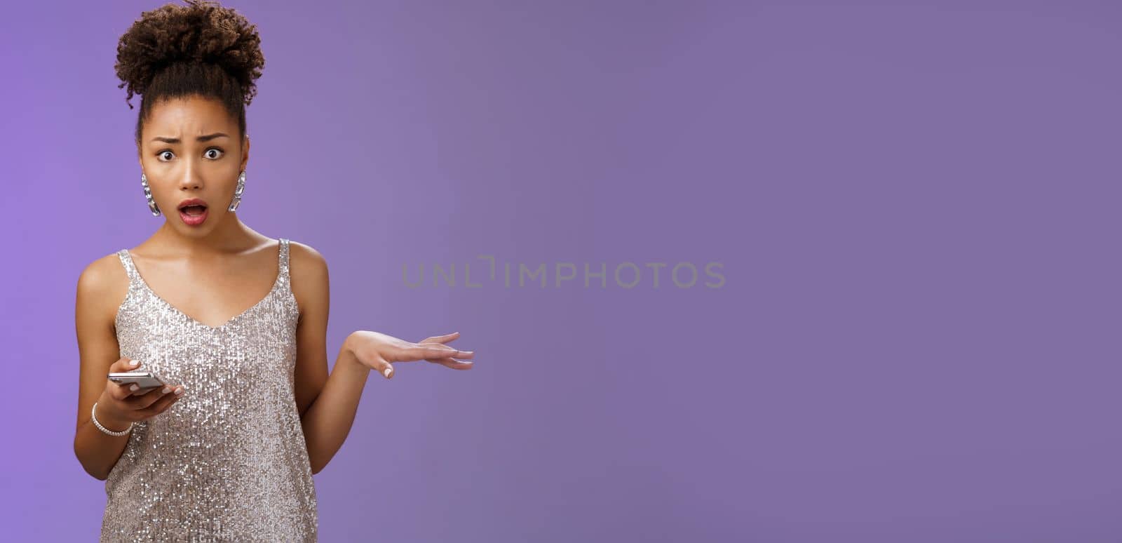 Concerned troubled arrogant silly glamour african american woman raise hand questioned holding smartphone insulted during phone call standing frustrated upset bothered blue background.