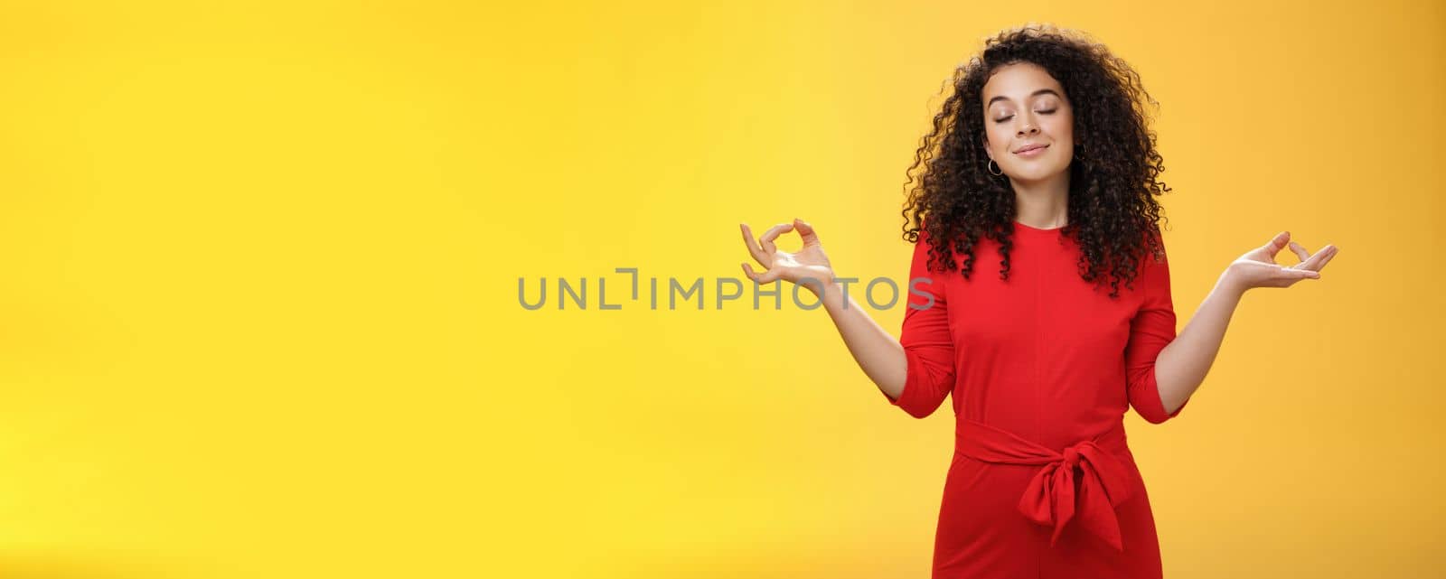 Charming dreamy and happy peaceful woman in red dress with curly hair standing in lotus pose with mudra orbs or zen gesture and closed eyes, meditation relieving stress, feeling unbothered by Benzoix