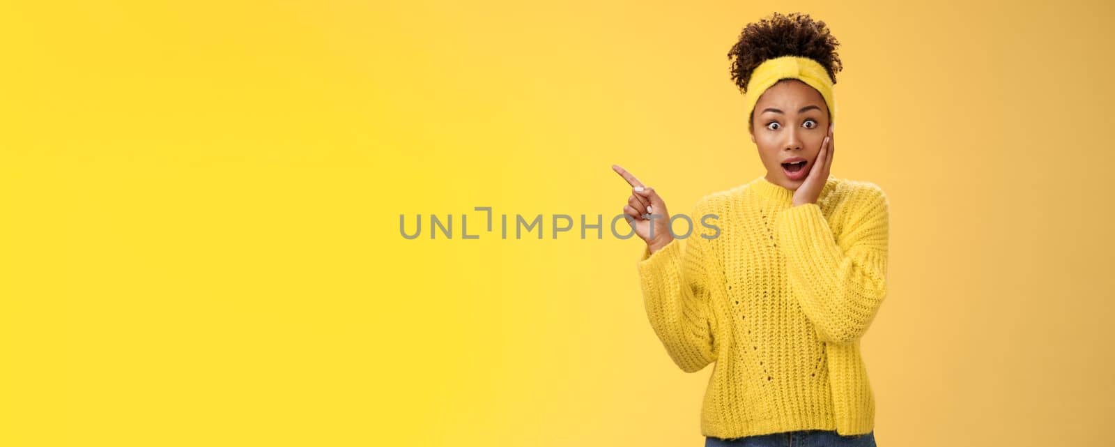 Shocked impressed emotive african-american girl afro hairstyle. gasping amazed touch cheek stunned widen eyes pointing upper left corner surprised telling you unbelievable discovery yellow background.