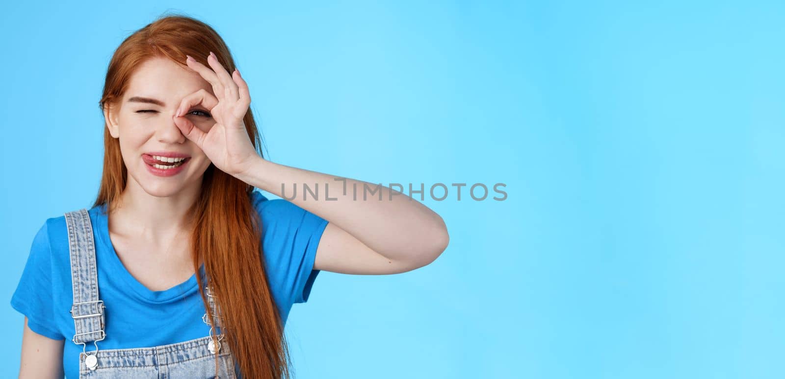 Playful lovely redhead female long red hairstyle, look through fingers carefree joyful, smiling show tongue sassy, enjoy summer vacation, stand blue background, tourist relax resort. Copy space