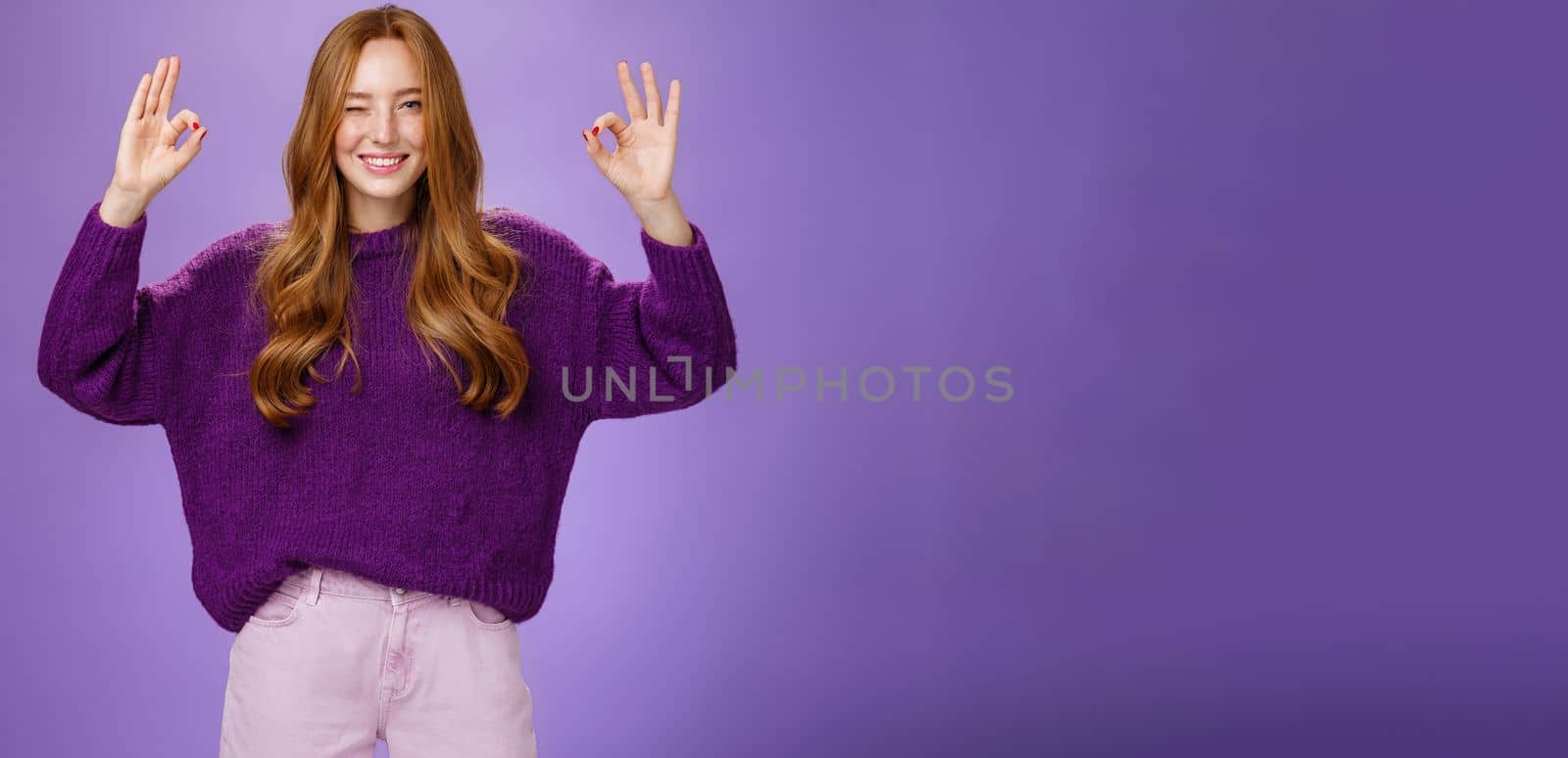 Relax everything ok. Assured charming and happy young redhead with long beautiful hair and freckles winking joyfully smiling and showing okay gestures with raised hands, affirming everything perfect by Benzoix