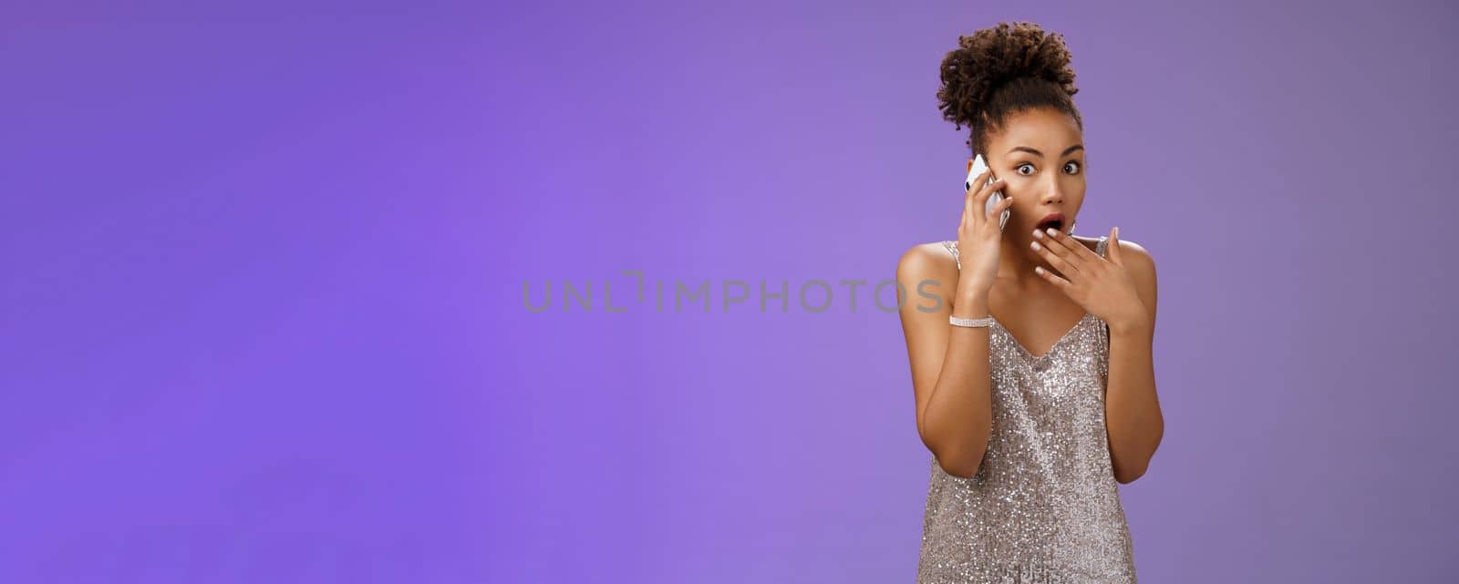 Impressed wondered african-american woman drop jaw gasping cover opened mouth gossiping hear amazing shocking rumor talking smartphone look speechless concerned camera, blue background by Benzoix