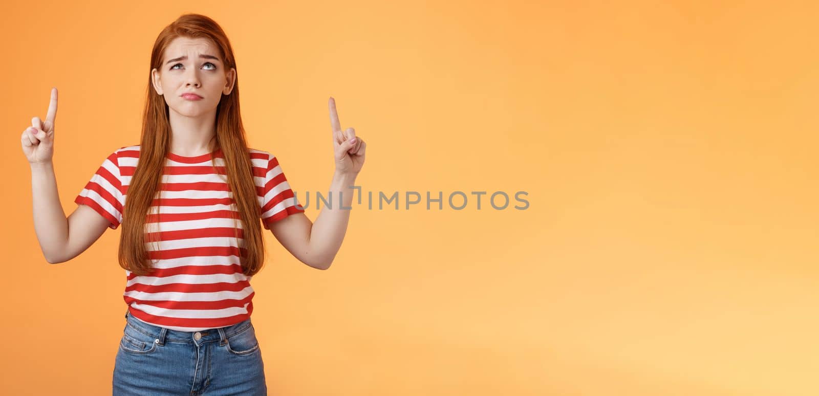 Hesitant upset cute redhead woman weighing choices look doubtful uncertain, frowning thoughtful, ponder decision, look pointing up unsure, have doubts, stand insecure orange background.