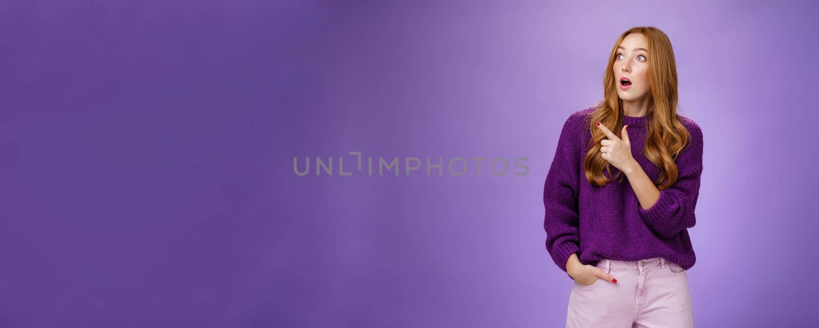 Girl surprised and thrilled as seing unbelievable scene. Portrait of impressed and shocked good-looking ginger woman in purple sweater gasping from amazement pointing, looking left intrigued.