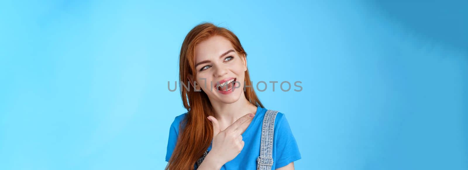 Sassy good-looking dreamy redhead female student contemplate cool performance, tilt head joyfully pointing look left, discuss holiday plans, curiously asking question, posing blue background.