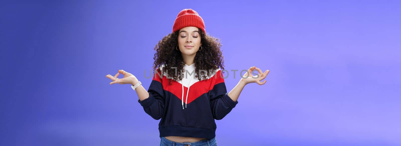 Waist-up shot of girl reaching nirvana feeling peaceful and calm holding hands sideways with mudra gesture close eyes, meditating releasing stress standing calm in lotus pose over blue background.