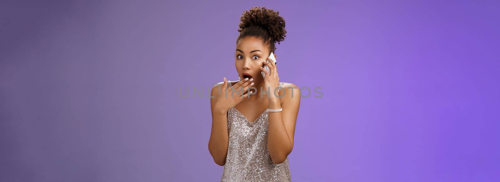 Impressed wondered african-american woman drop jaw gasping cover opened mouth gossiping hear amazing shocking rumor talking smartphone look speechless concerned camera, blue background by Benzoix