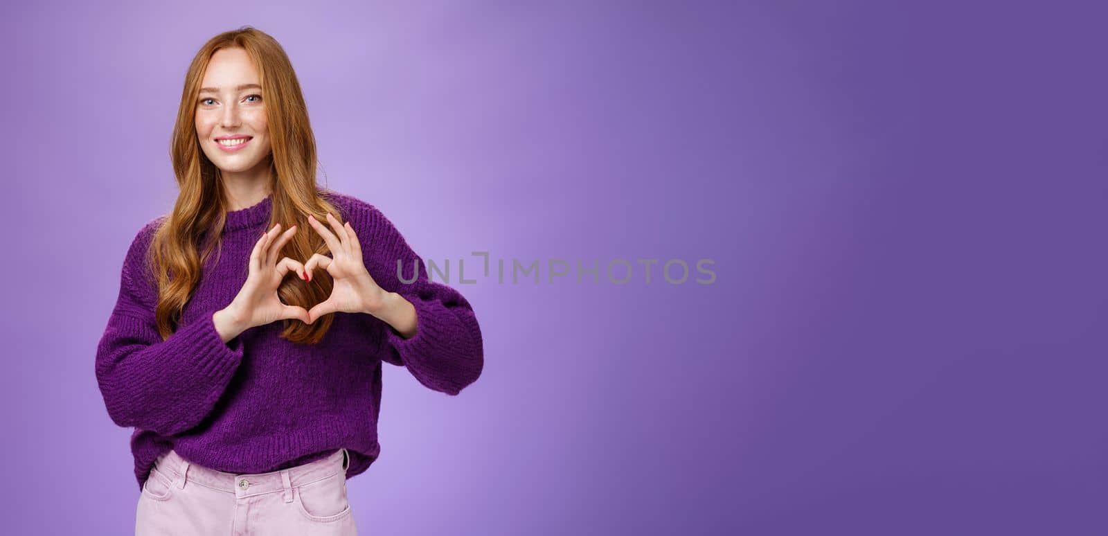 Girl loves new place to hang out, showing heart gesture and smiling satisfied and cute, expressing sympathy and admiration looking romantic and dreamy against purple background.