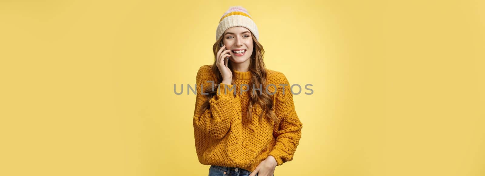 Carefree sociable good-looking outgoing woman calling friend talking happily smartphone have pleasant funny conversation smiling giggling look away hold hand pocket, standing yellow background by Benzoix