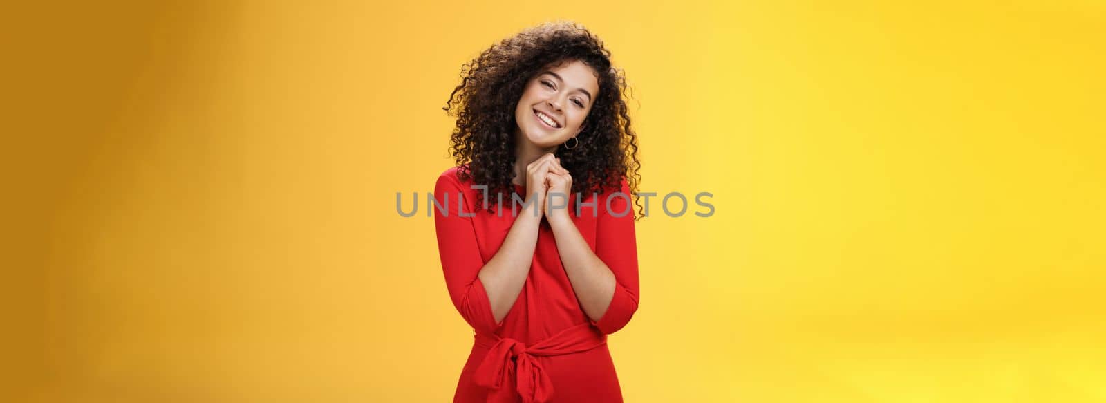 So sweet love you. Portrait of tender and silly cute curly-haired young woman in red dress tilting head holding hands together near face and smiling touched during heartwarming moment of confession by Benzoix