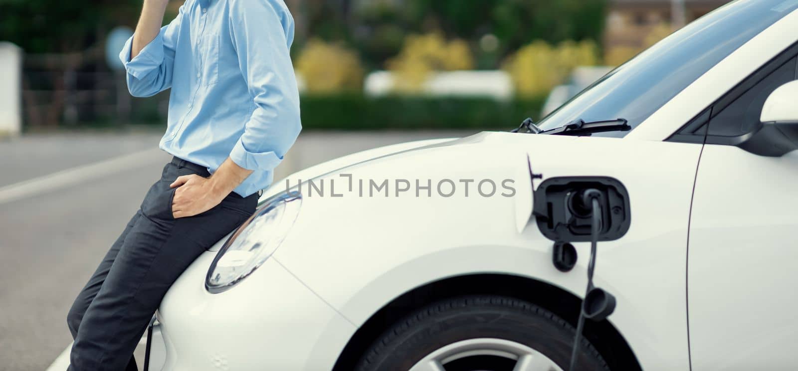 Closeup progressive businessman with electric vehicle at charging station. by biancoblue