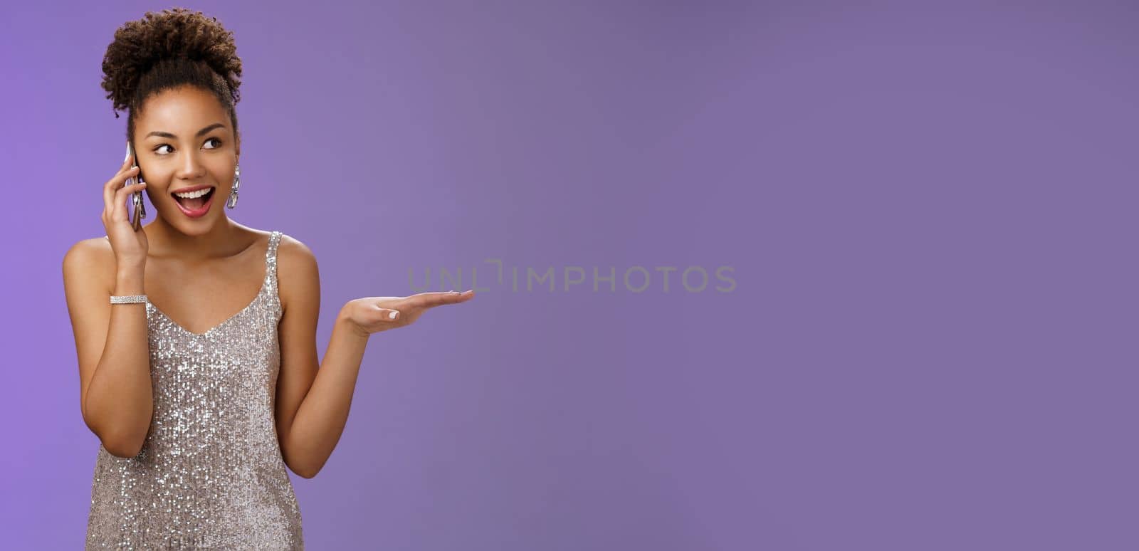 Talkative sociable attractive elegant african-american woman in glittering silver dress gesturing describing party talking smartphone look up amused have nice friendly conversation, blue background.