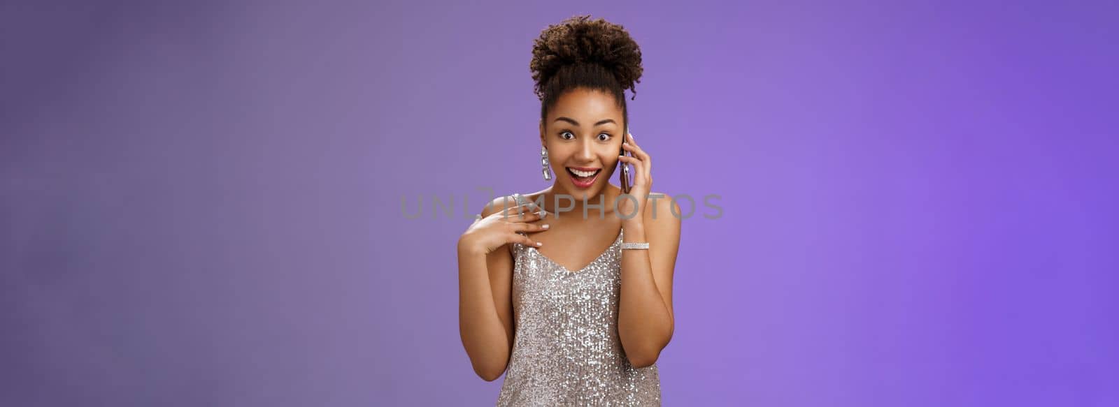 Impressed talkative charming african-american woman in shiny silver evening dress pointing herself amused surprised smiling talking smartphone widen eyes astonished, standing blue background.