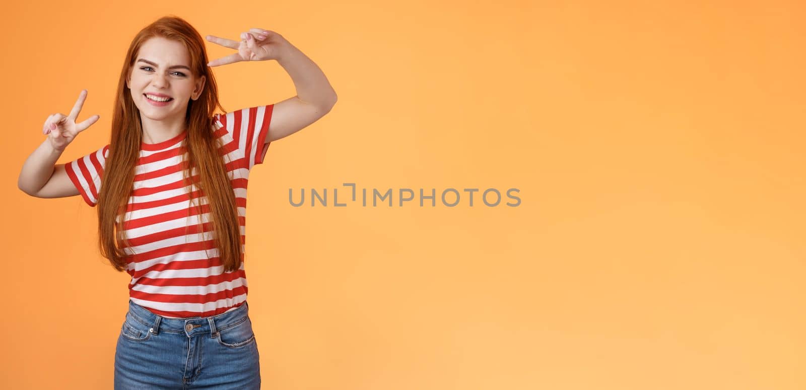 Friendly upbeat good-looking redhead woman rejoicing, feel happy, enjoy summetime, take first photo vacation, send coworkers summer shot, make peace victory signs, smiling broadly orange background.
