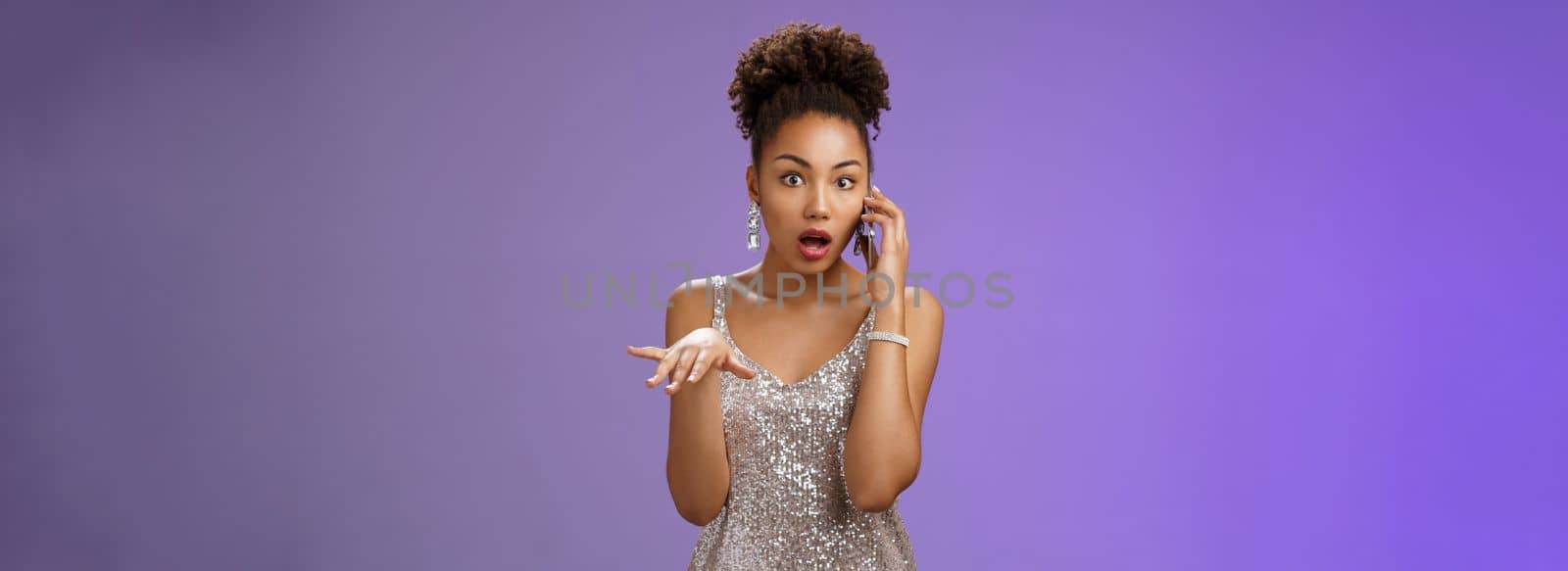 Astonished shocked african american woman gossiping talking smartphone drop jaw astonished holding phone ear raise hand dismay concerned standing speechless hear rumour, standing blue background.