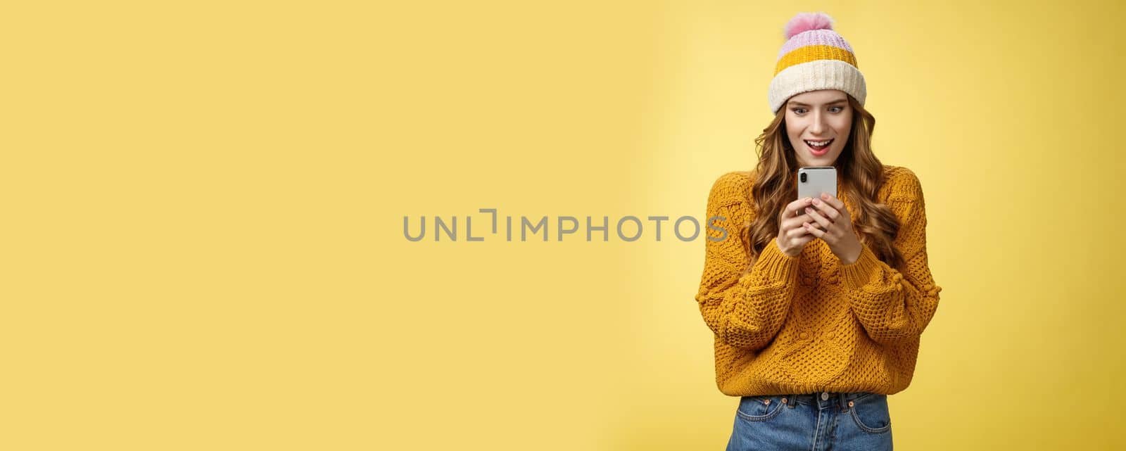 Amazed attractive stylish woman receive message smartphone awesome promotion ready shopping online smiling thrilled excited look mobile phone display, posing yellow background. Technology concept