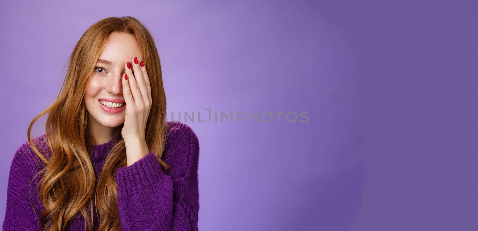 Cute and tender redhead girl checking sight at optician closing one eye as reading words smiling broadly feeling relaxed as being in hands of professional ophthalmologist over purple background. Sight, health and patient concept