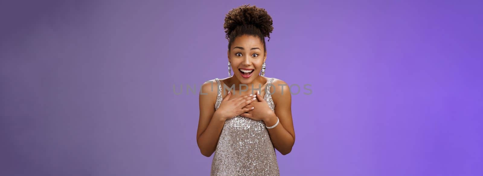 Amused happy grateful charming african-american woman in evening silver dress press palms chest thankful smiling broadly appreciating awesome touching heartwarming gift, standing blue background.