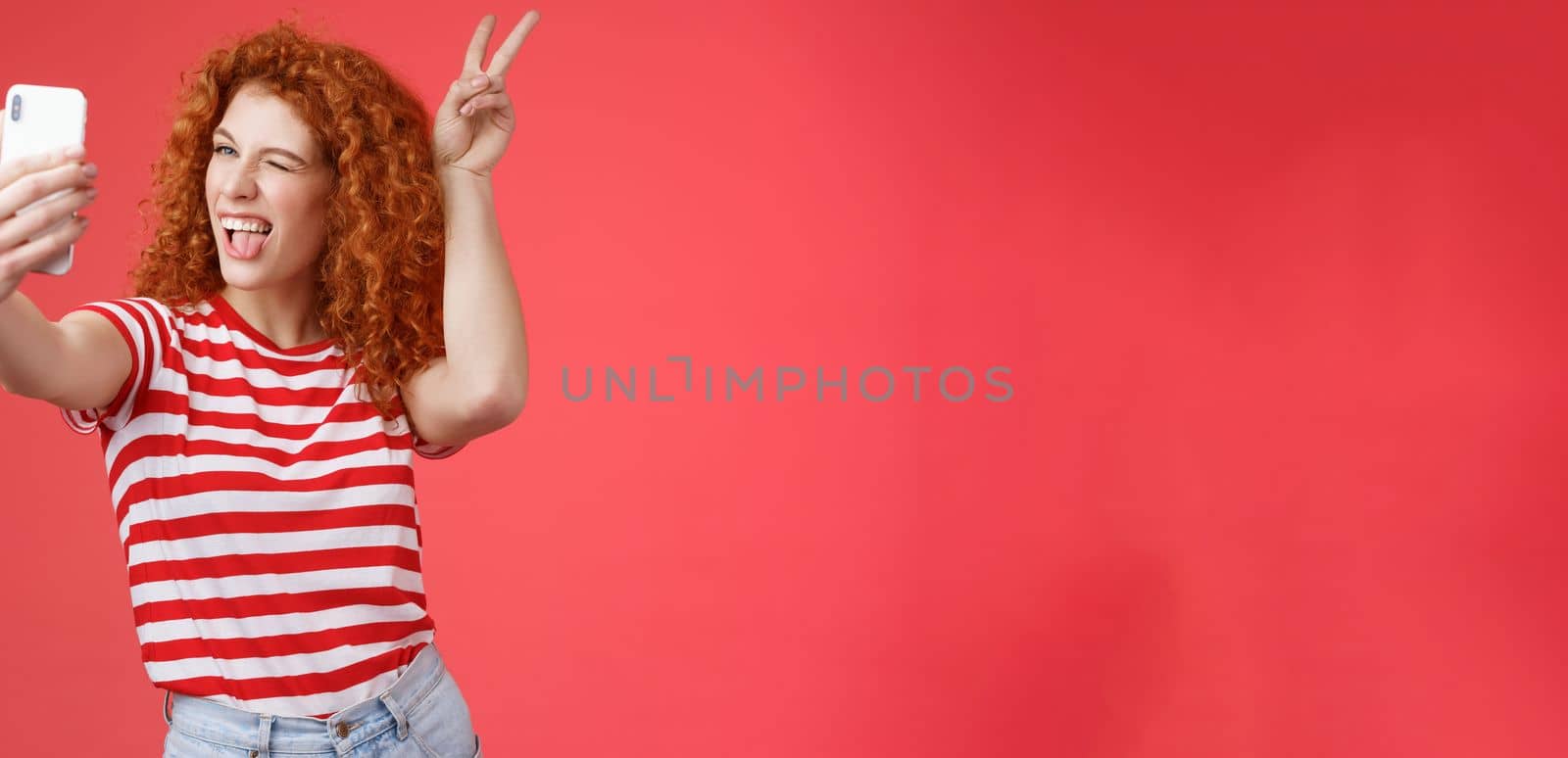 Lifestyle. Sassy fashionable playful good-looking redhead daring curly woman show peace victory animal ears gesture winking smartphone display record vlog taking selfie awesome phone camera red background.
