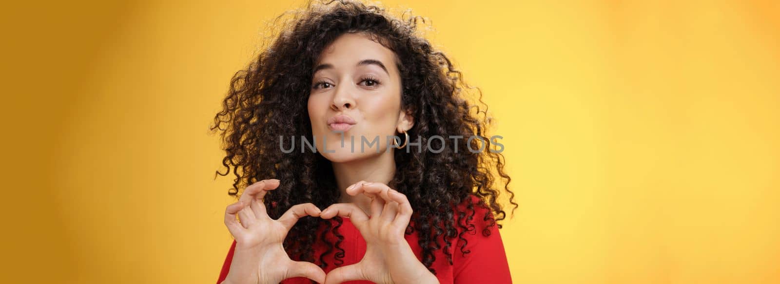 Close-up shot of romantic and tender young girlfriend with curly hair folding lips in kiss or mwah showing heart gesture, expressing love and romance, confessing in admiration or sympathy by Benzoix