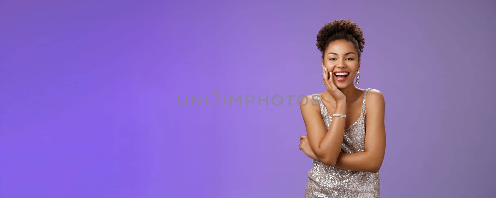 Charming joyful glamour african-american woman in glittering dress touch palm laughing happily attend elegant party chatting enjoying fun event chuckling rejoicing good mood, blue background.