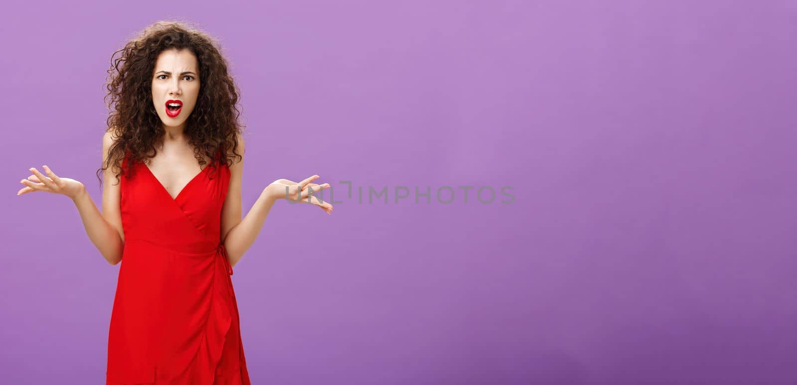 Woman being shocked guy breaking up with her during party. Concerned pissed and outraged good-looking lady in red dress with evening makeup shrugging with spread palms in clueless and questioned pose.