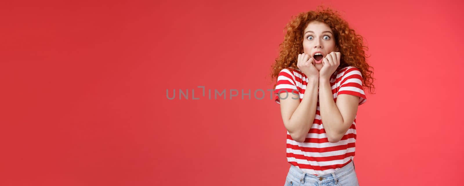 Shocked scared ambushed redhead curly-haired cute girlfriend insecure gasping drop jaw scream frightened stare camera hold hands opened mouth terrified standing stupor red background by Benzoix