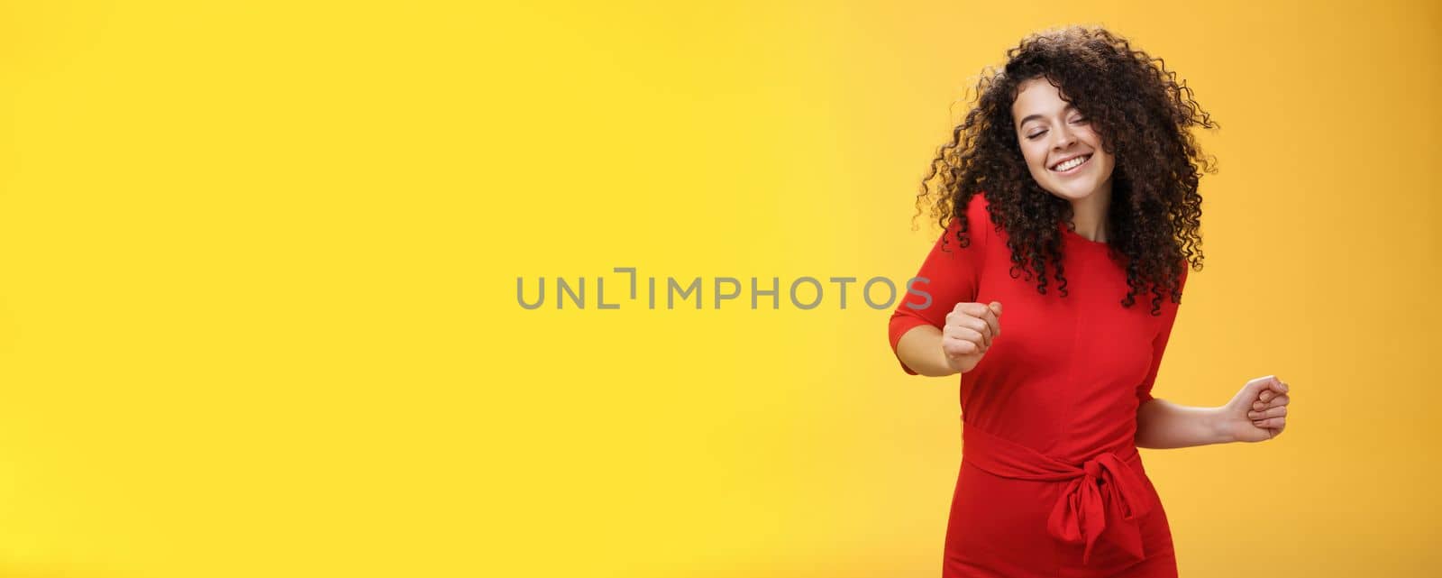 Carefree woman dancing on dance floor with close eyes and smile enjoying life feeling happy and joyful close eyes and making tender expression as moving to rhythm of music over yellow background. People, lifestyle and emotions concept
