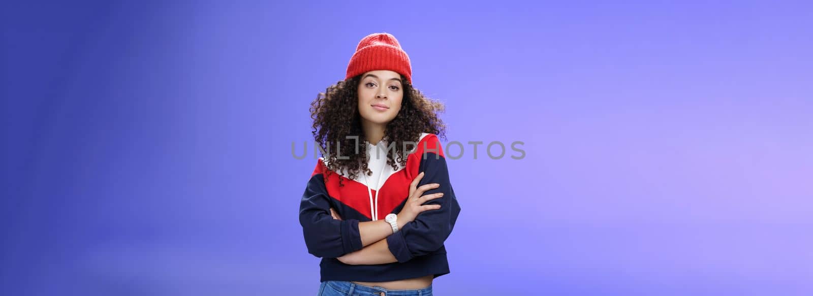 Girl will show winter who boss. Confident and stylish self-assured attractive woman with curly hair in cute red beanie and warm sweatshirt holding hands crossed over chest and looking daring at camera. Fashion, weather and people concept