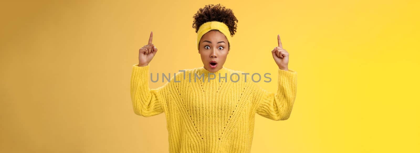Shocked surprised emotive african-american female student drop jaw widen eyes learn astonishing news pointing raised fingers up gasping concerned impressed, speechless standing yellow background by Benzoix