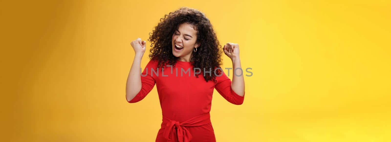 Lifestyle. Girl enjoying cool music feeling awesome as relaxing at party dancing and feeling awesome raising clenched fists saying yeah turning head joyfully with closed eyes having fun over yellow background.