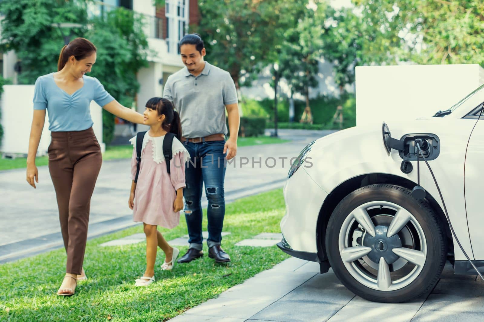 Progressive young happy family with electric vehicle and home backyard charging station. Green and clean energy from electric vehicles for healthy environment. Eco power from renewable source.