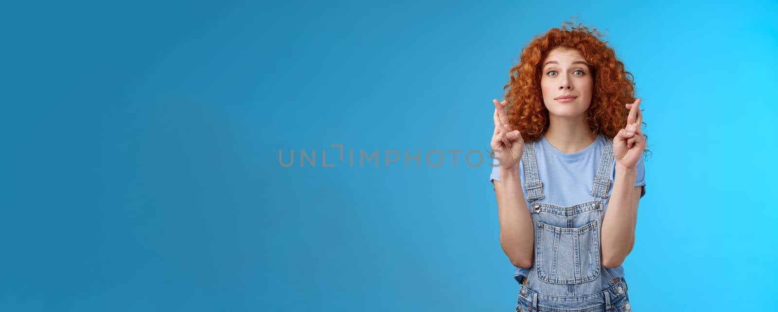 Hopeful relaxed optimistic cute european redhead curly girl smiling faithfully awaiting good results believe wish come true cross fingers good luck grin anticipating important news dream fulfill by Benzoix