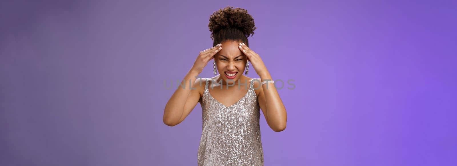 Pressured intense worried african-american woman in silver glittering dress grimacing cringing painful headache hold hand forehead suffer pain migraine, standing bothered blue background.