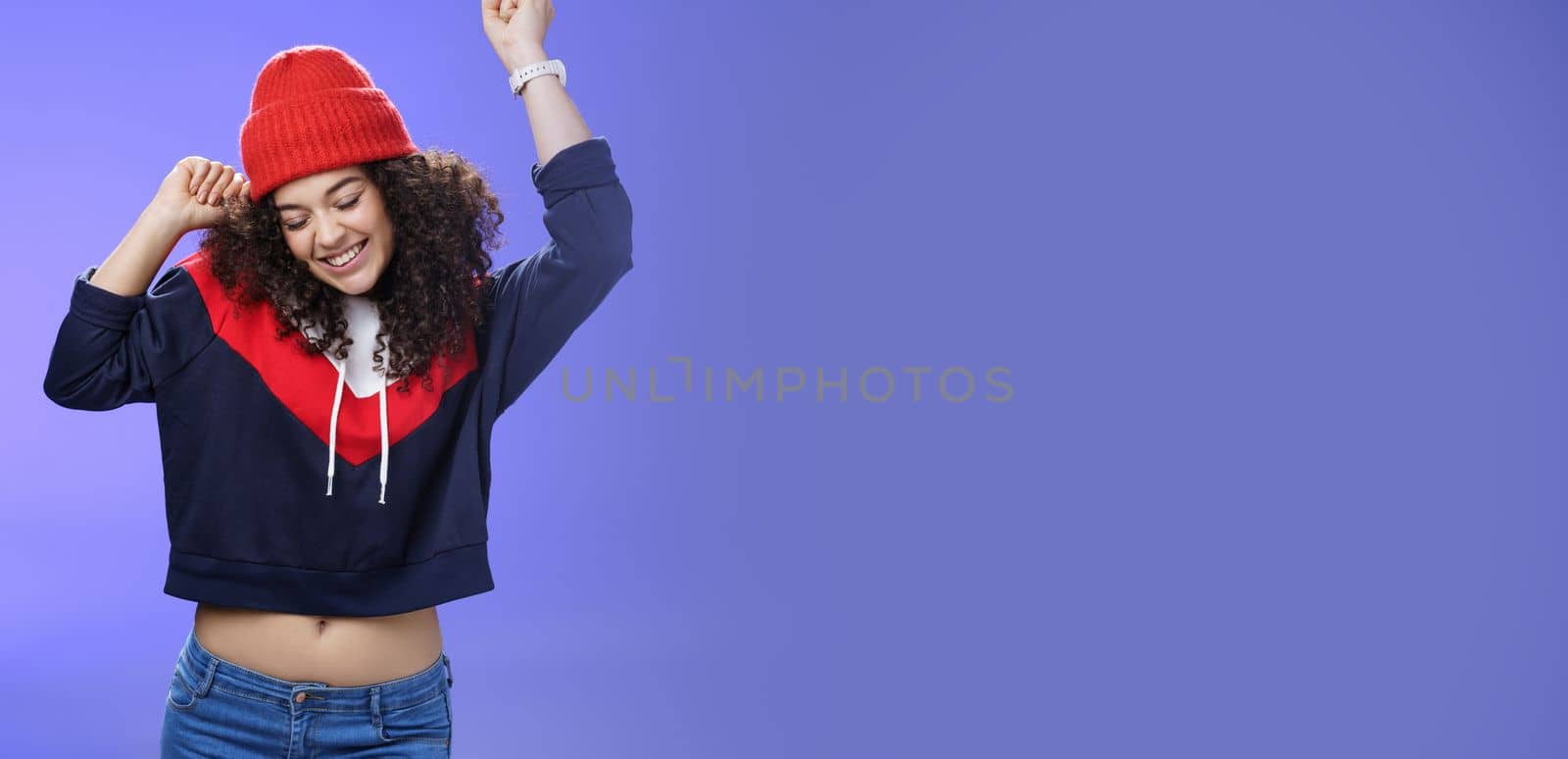 Girl celebrating favorite season in year. Portrait of carefree and joyful dancing woman with curly hair in cute red hat lifting hands in dance movements smiling enjoying music and holidays.