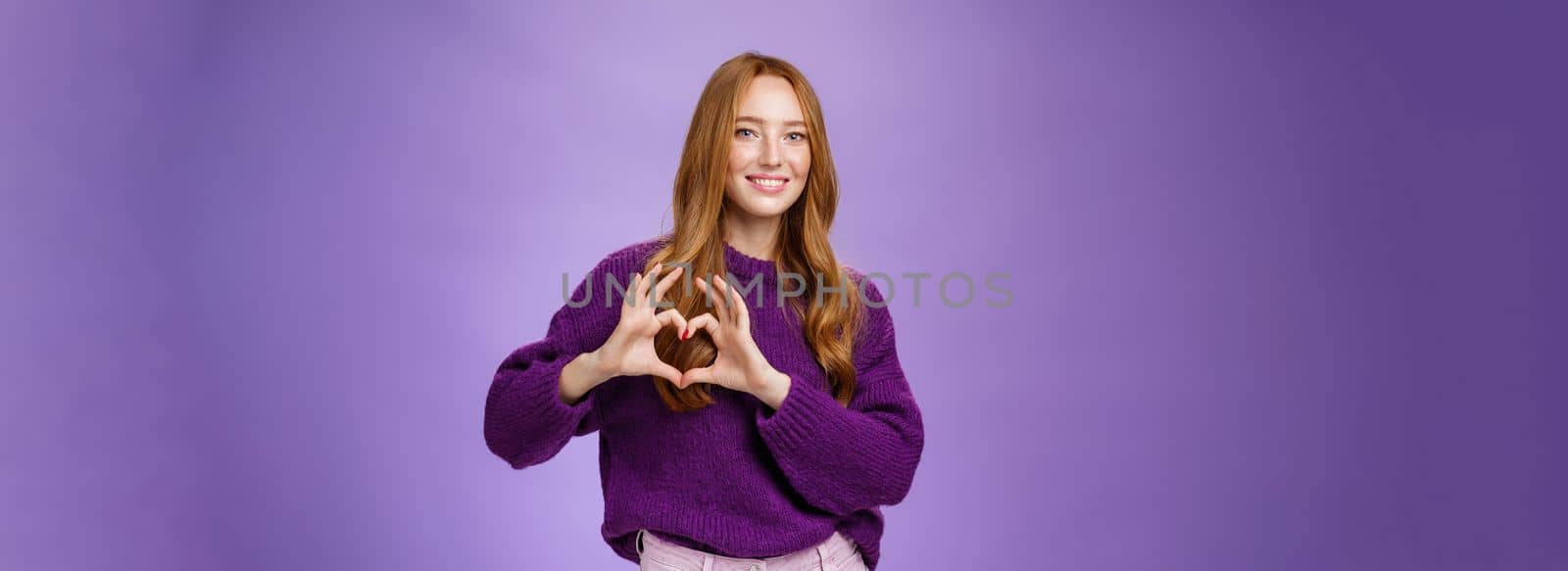 Girl loves new place to hang out, showing heart gesture and smiling satisfied and cute, expressing sympathy and admiration looking romantic and dreamy against purple background.