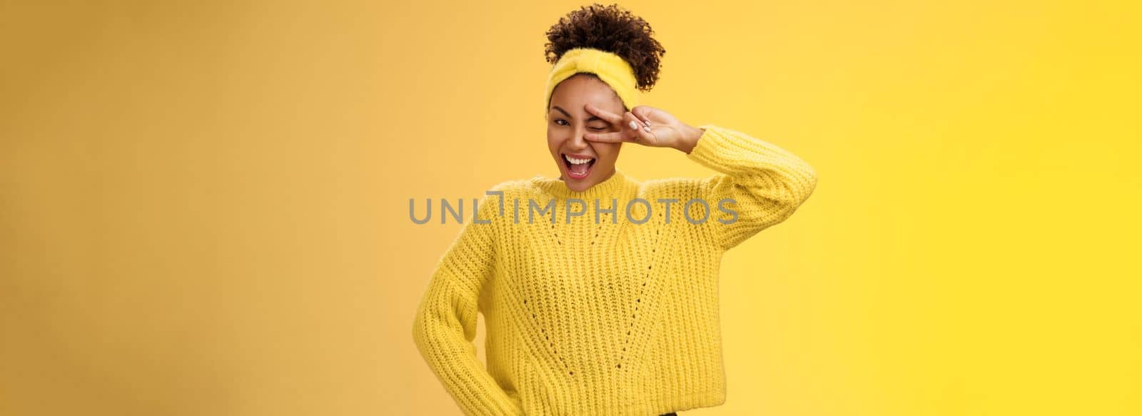 Friendly self-assured energetic african-american smiling healthy girl winking positive attitude grinning cheerful show peace victory lucky gesture hold hand waist confident, yellow background.