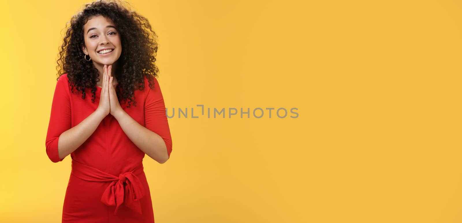 Girl with angel smile making eyes as wanting friend make favour, holding hands in pray, grinning and gazing with anticipation as begging for help standing silly and cute against yellow background by Benzoix