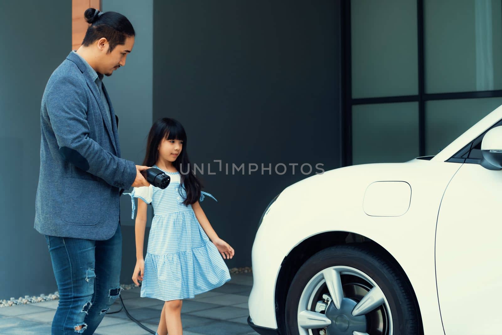 Progressive concept of father and daughter with EV car and home charging station by biancoblue