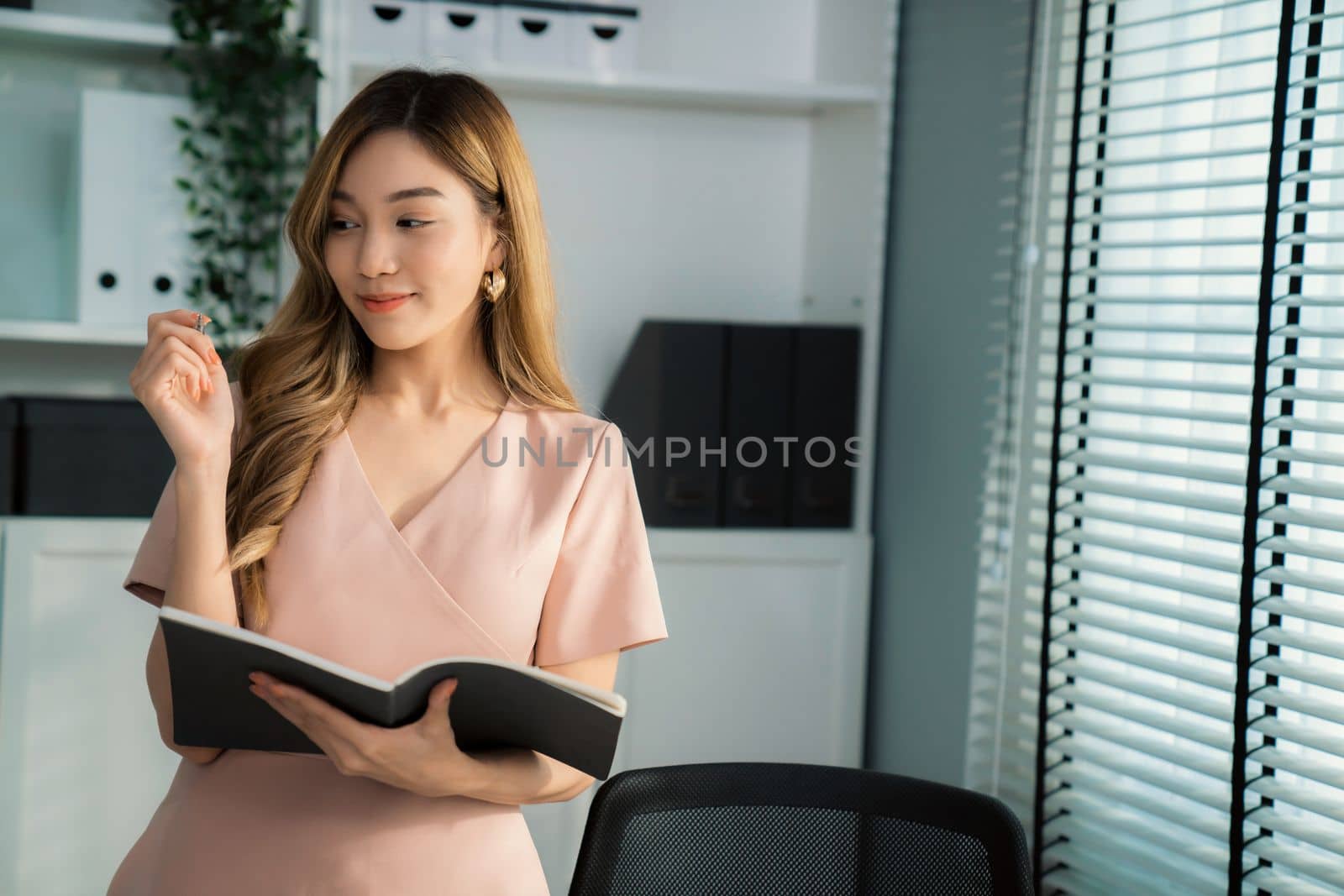Young competent office lady, intern, secretary holding a log in office room. by biancoblue