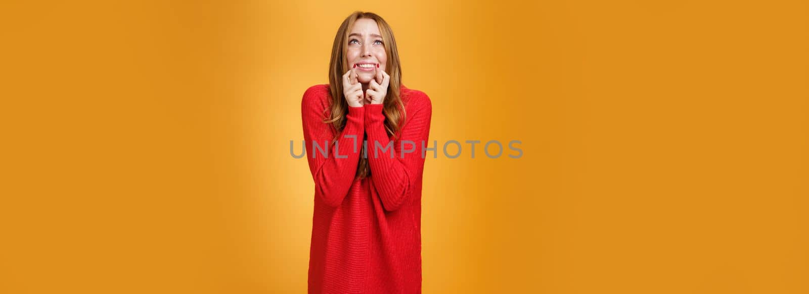 Lifestyle. Portrait of excited and worried young redhead female in 20s stooping standing in begging pose crossing finger for good luck looking at sky as praying god and asking help with wish come true.