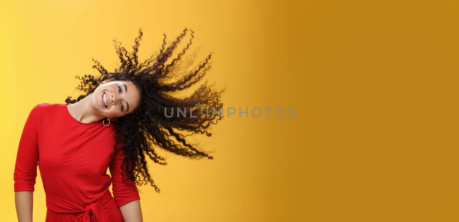 Girl getting carefree and wild waving hair and making sun with curls flying in air smiling broadly tilting head and having fun, dancing delighted and amused feeling playful against yellow background by Benzoix