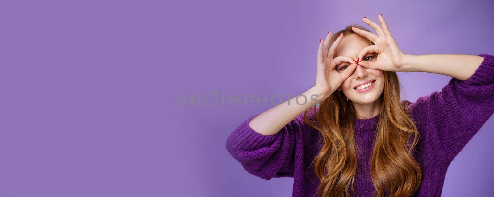 Hey smile more. Portrait of bright and funny charming redhead girl in purple sweater making mask with hands over eyes and smiling broadly acting like superhero posing excited and playful.