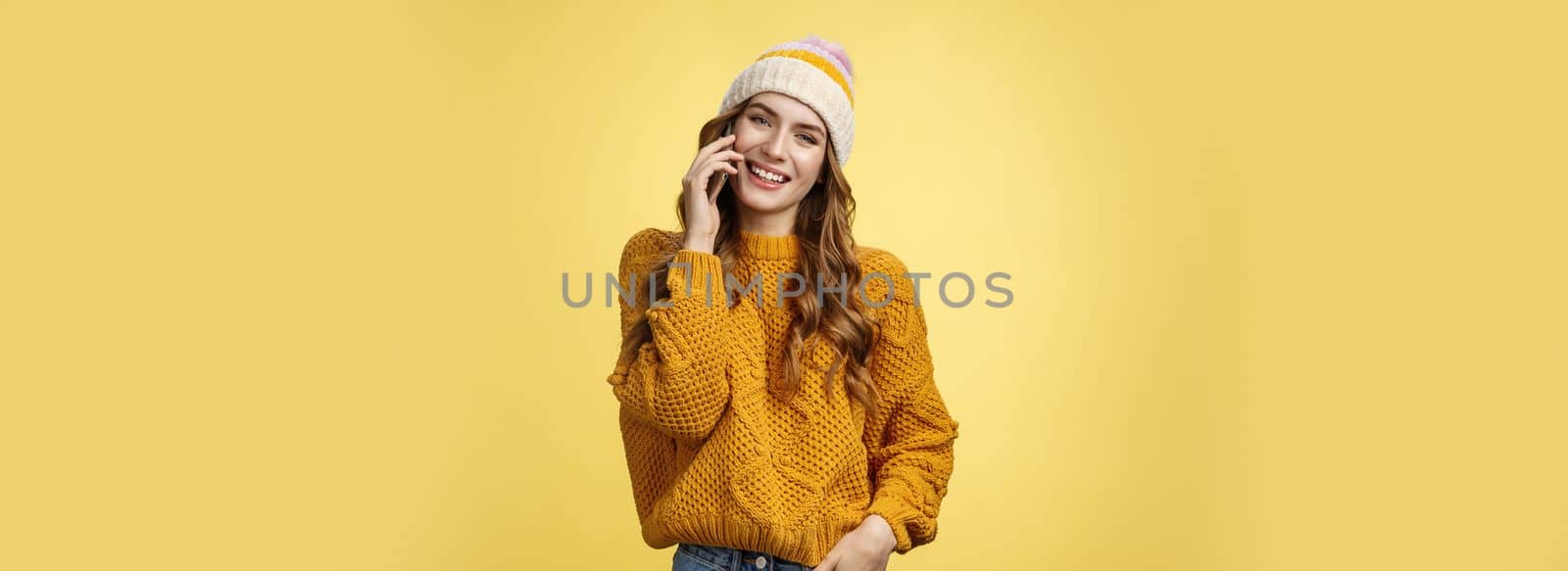 Charming stylish european woman wearing hat sweater tilting head flirty smiling talking smartphone calling boyfriend consulting friend via cellphone, standing happily casual pose yellow background by Benzoix