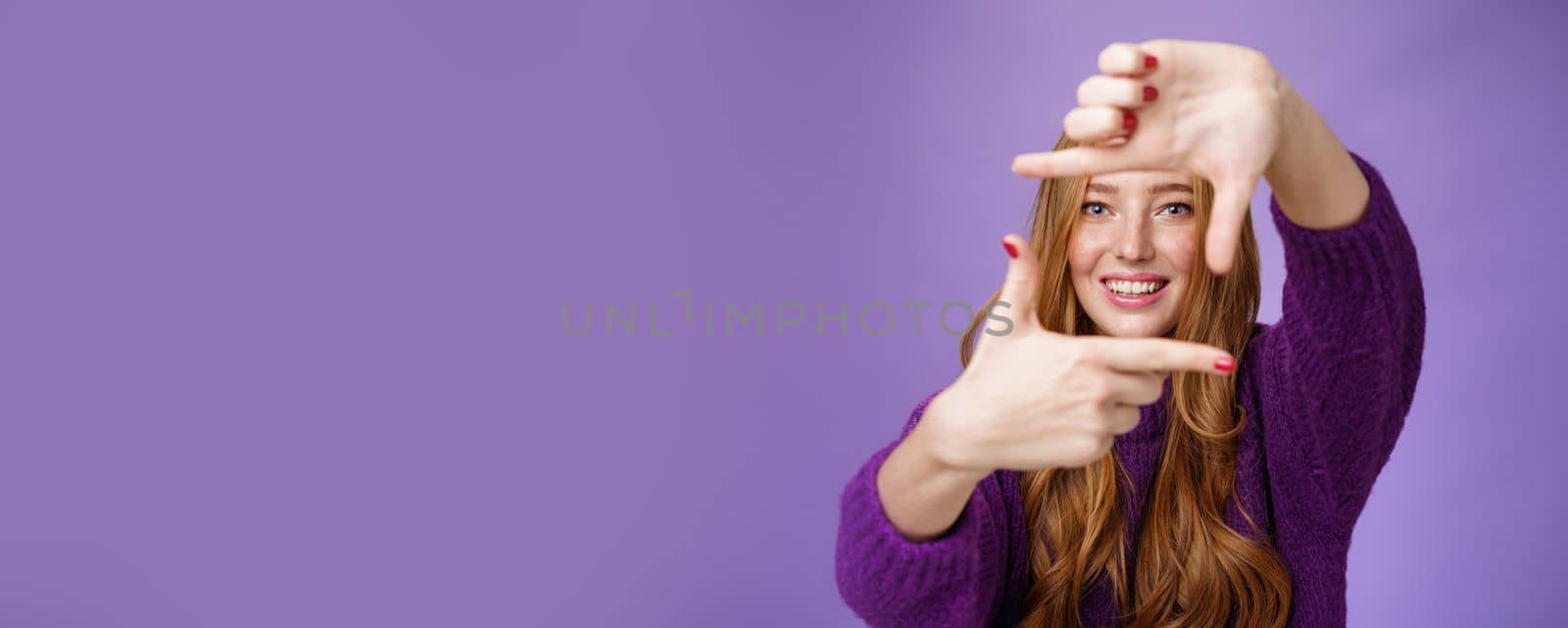 Imagine if. Portrait of hopeful and carefree creative charming redhead 20s woman showing frame with pulled hands and smiling through it as picturing bright and happy future over purple background.