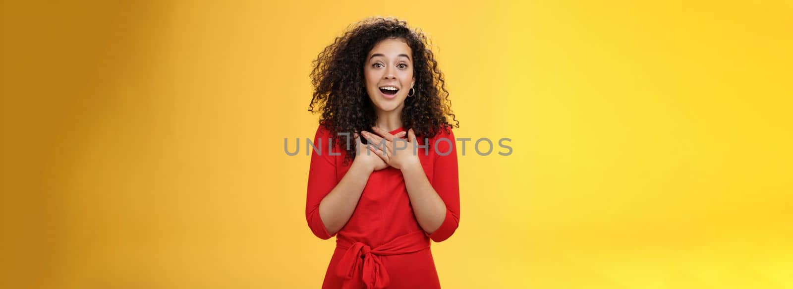 Charming girlfriend receiving new year present feeling happy and surprised holding hands on chest sighing and smiling broadly from amazement, being thankful and glad over yellow wall by Benzoix