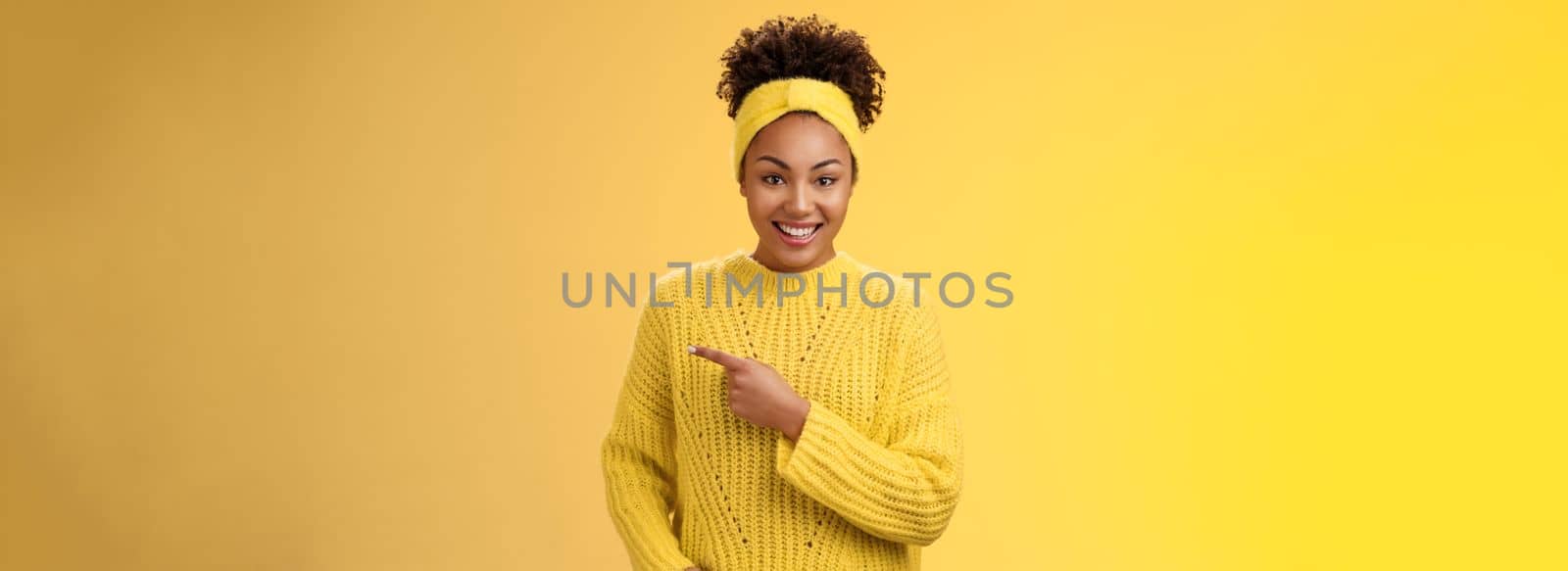 Friendly ougoing relaxed african-american woman casually pointing right during conversation discussing recent new cafe open awesome discounts promos standing happily yellow background. Copy space